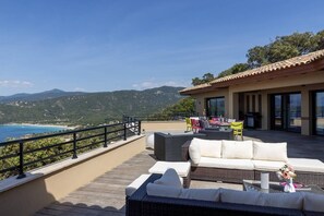 Um terra ço com mobiliário externo, área de refeições e vista para o mar e montanhas.
