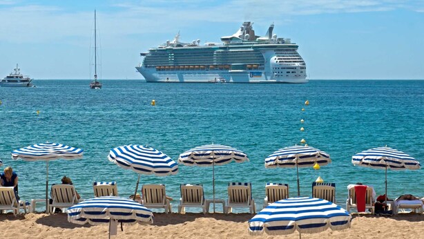 Un navire de croisière était amarré sur une plage où se trouvaient de nombreux parasols et des chaises de plage aux rayures bleues et blanches.