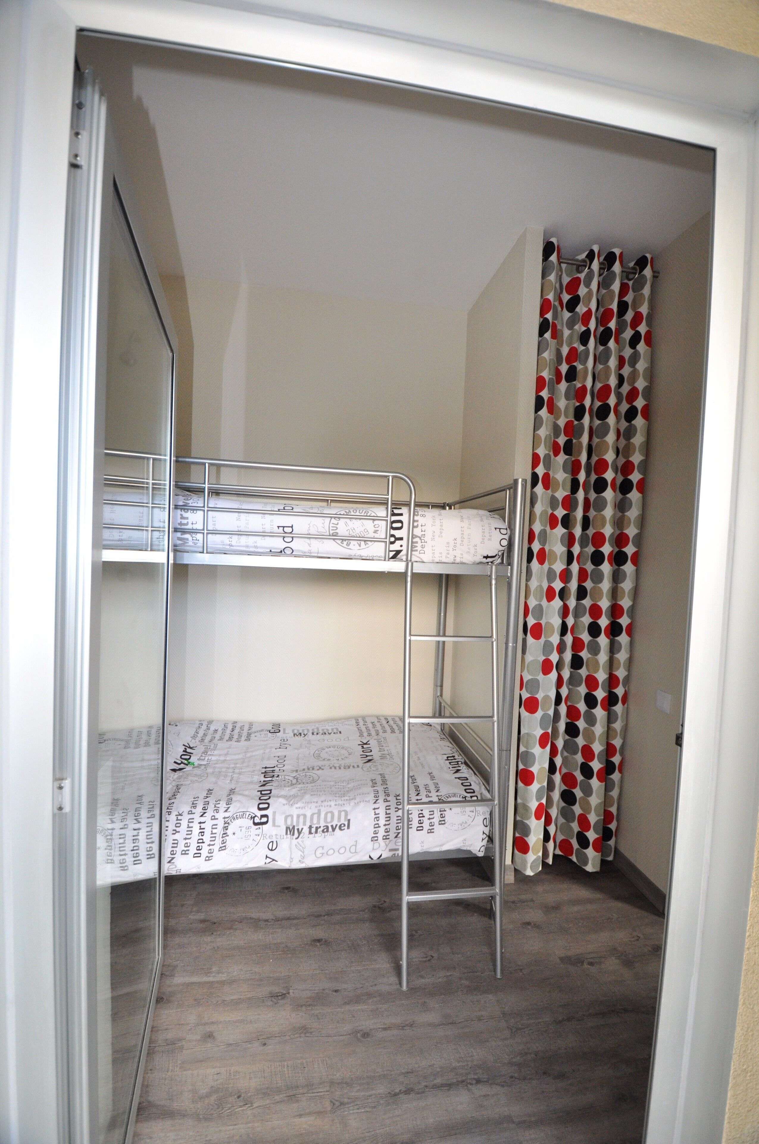 A room with a bunk bed, a metal ladder, and a curtain with a polka dot pattern.