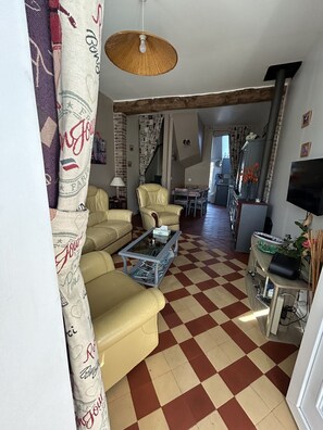 A living room with a checkered floor, a glass coffee table, leather sofas, a hanging lamp, and a television.
