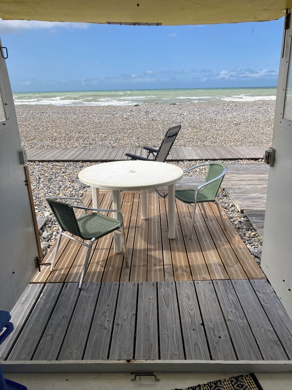 A wooden deck with a table and chairs overlooking a pebble beach.