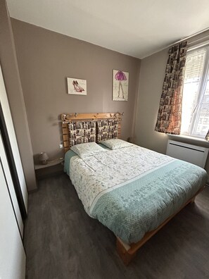 A bedroom with a bed, a headboard with a photo collage, a window with curtains, and a wall with two framed pictures.