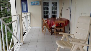 A covered patio with a tiled floor, a table with chairs, a door, and a railing. - GÎTE LES PIMENTIERS DE PAPAYE (Saint Claude)