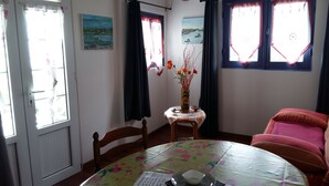 A dining area with a round table covered by a floral tablecloth, a vase with flowers, and a chair with a red cushion. - GÎTE LES PIMENTIERS DE PAPAYE (Saint Claude)