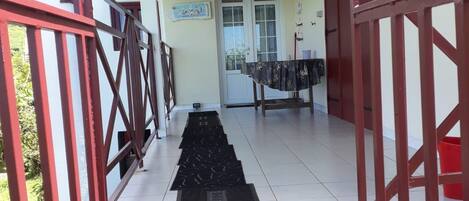 Un espace extérieur abrité, doté d’un escalier en métal menant à une porte, d’un sol carrelé et d’une rambarde en métal rouge.