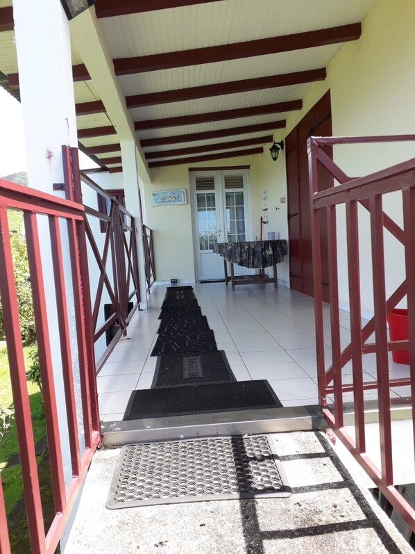 A covered outdoor area with a metal staircase leading to a door, a tiled floor, and a red metal railing.