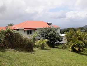 A house with a red roof, surrounded by lush greenery and a clear sky.