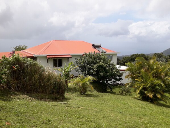 A house with a red roof, surrounded by lush greenery and a clear sky.