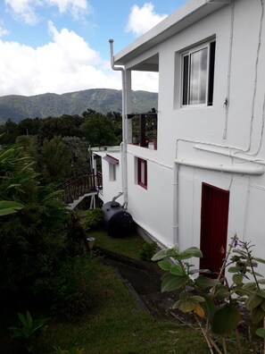 A white building with a red door, a balcony, and a view of a mountainous landscape.
