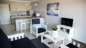 A modern living room with a sofa, coffee table, and TV stand. There is a kitchen area with a microwave and cabinets.