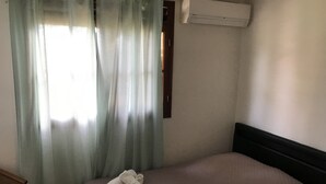 Een slaapkamer met een bed, een stoel, een raam met gordijnen en een airconditioning.