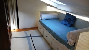 Una habitación pequeña con cama individual, tragaluz, ventana y un diseño sencillo y limpio.