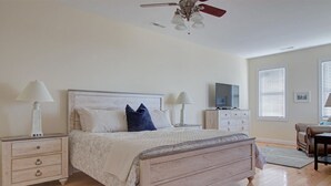 Ein Schlafzimmer mit einem Bett, zwei Nachttischen, einem Deckenventilator, einem Fernseher und einem Fenster mit Jalousien.