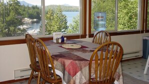 A dining area with a table set for four, overlooking a lake with boats and trees.