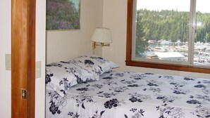 A bedroom with a bed, a window with a view of a marina, and a lamp.