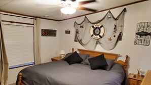 Un dormitorio con una cama grande, cabecera de madera, una mesita de noche con lámpara y decoración náutica en la pared.