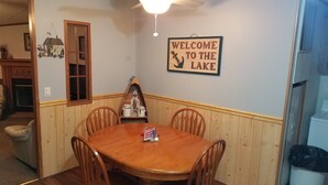 Un comedor con mesa y sillas de madera, un ventilador de techo y un cartel en la pared que dice 'Welcome to the Lake'.