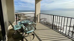 Ein Balkon mit Tisch und Stühlen mit Blick auf Strand und Meer.
