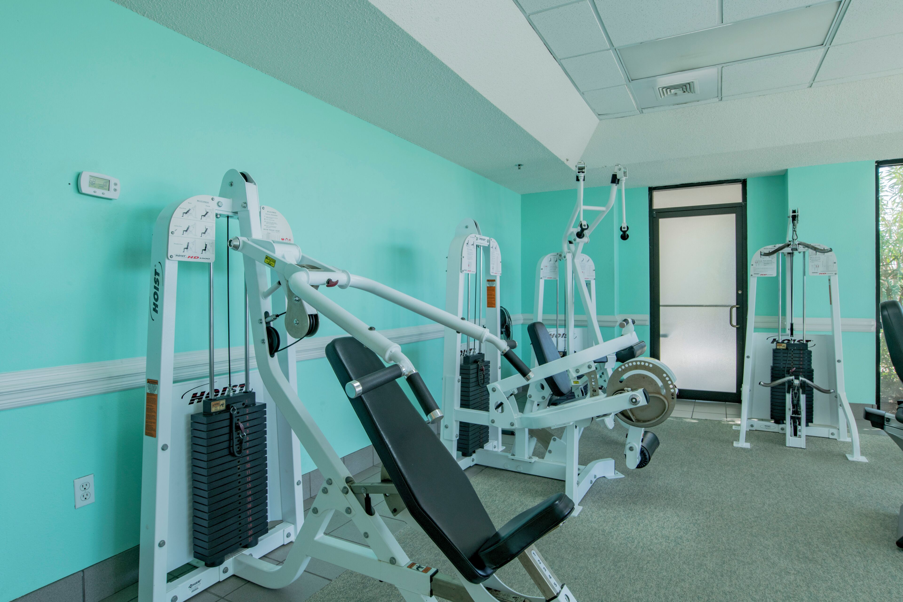 Une salle de sport équipée de divers appareils d’exercice, avec une porte et une fenêtre.