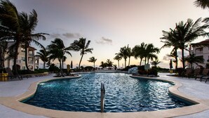 Ein Pool mit gewölbter Kante, umgeben von Palmen und Liegestühlen.