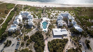 Eine Luftaufnahme eines Resorts mit mehreren Gebäuden, einem zentralen Pool und einem Strand.