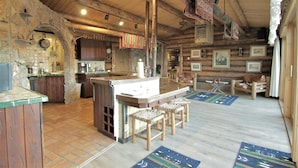 A rustic cabin interior with a stone archway, wooden ceiling beams, a central island with stools, and a fireplace. - Large, Private & Charming retreat is ultimate upscale stay near Cody, Y.S. Park (Ralston)