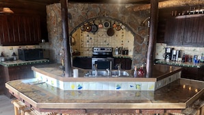 A kitchen with a central island, wooden stools, and a stone backsplash. - Large, Private & Charming retreat is ultimate upscale stay near Cody, Y.S. Park (Ralston)