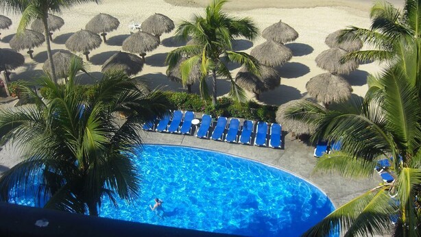 Une vue sur la piscine, avec une plage, des palmiers et des chaises longues.
