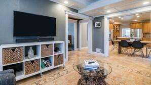 A modern living room with a flat-screen TV, a glass coffee table, and a dining area with a wooden table and chairs.