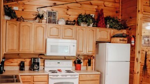 A wooden cabin kitchen with wooden cabinets, a white stove, a microwave, and a refrigerator. - "Sweet Life" Log Cabin Creekside, Trout Fishing, Foosball, Hot Tub and Firepit (Cosby)