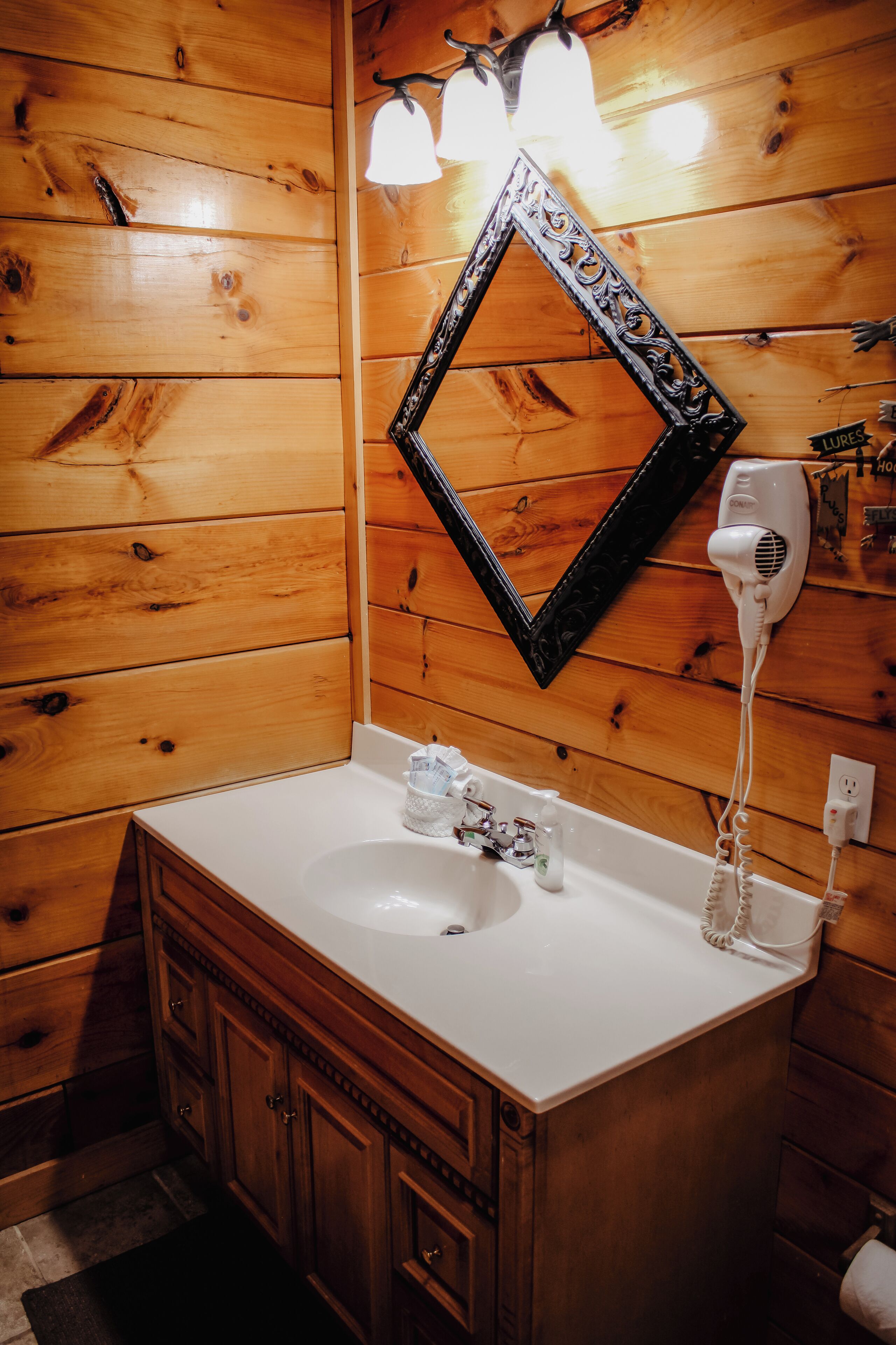 Une salle de bain rustique, avec une cabine en bois, un lavabo blanc, des meubles en bois, un miroir et un sèche-cheveux.