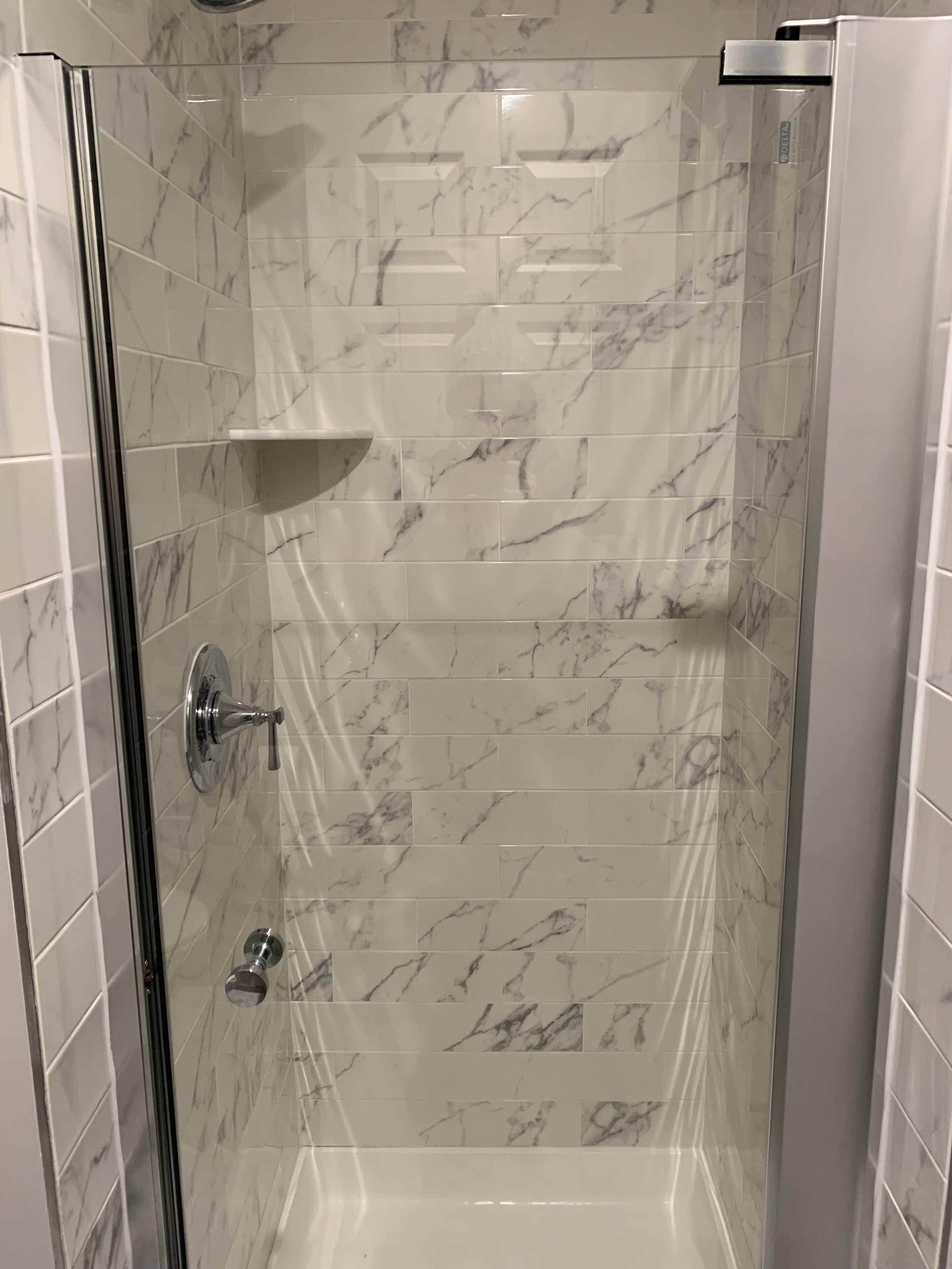 Ducha con puerta de vidrio, azulejos de mármol y grifo de cromo.