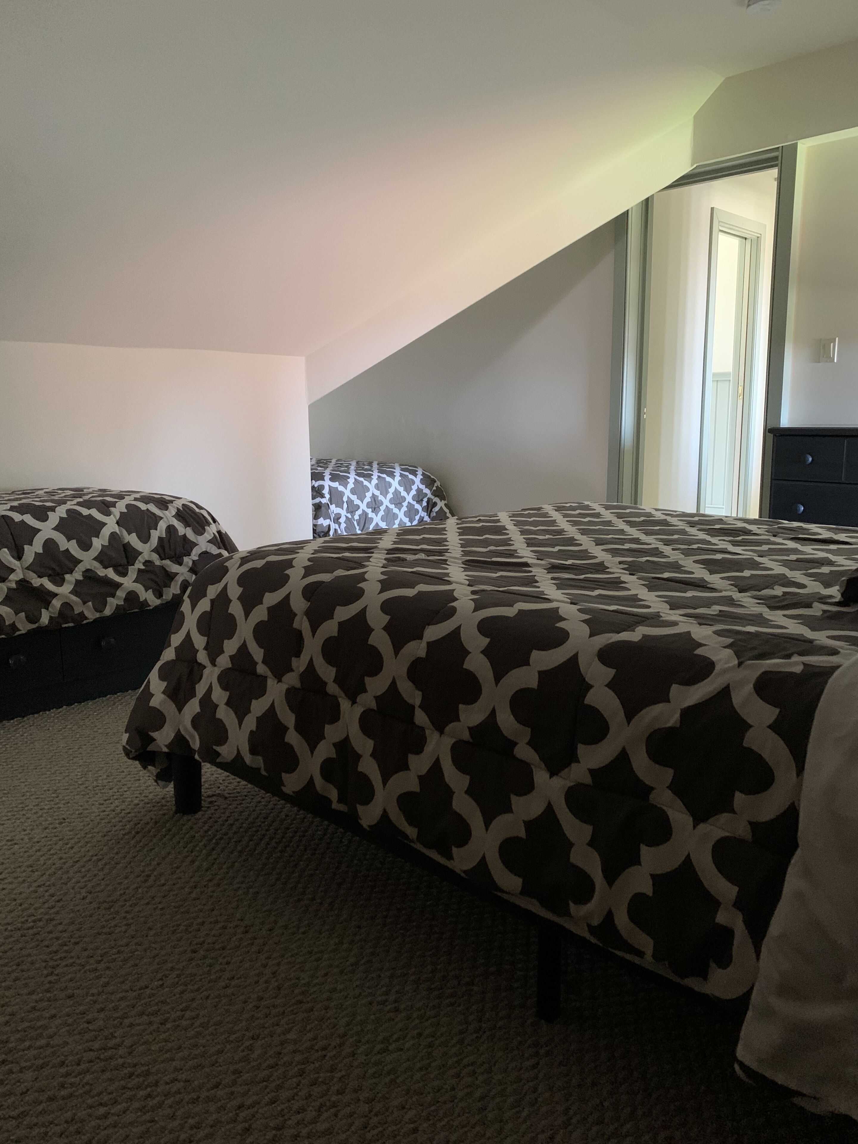 A bedroom with two beds, a dark wooden dresser, and a door leading to another room.