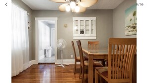 Un comedor con mesa y sillas de madera, ventilador de techo y ventana con vista al exterior.