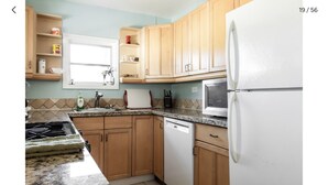 Una cocina con armarios de madera, un refrigerador blanco, un microondas y un lavamanos con una ventana encima.