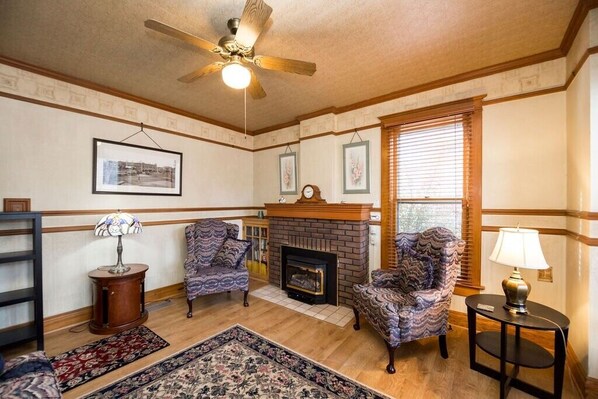 A living room with a fireplace, patterned armchairs, a ceiling fan, and a rug.
