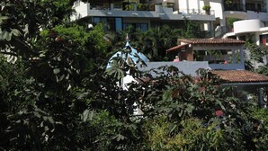 Un hotel de varios pisos con balcones, una estructura de techo de paja y abundante vegetación.