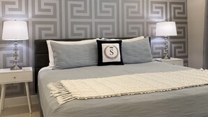 A bedroom with a bed, two bedside tables, and a patterned wall. - WEEKLY or MONTH TO MONTH LUXURY VACATION RENTAL - AP1  (Pompano Beach)