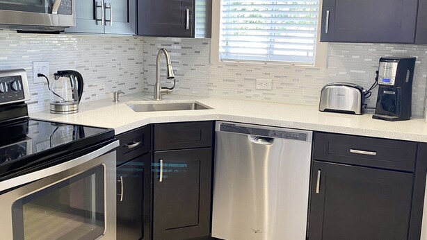 A modern kitchen with stainless steel appliances, dark cabinetry, and a tiled backsplash. - WEEKLY or MONTH TO MONTH LUXURY VACATION RENTAL - AP1  (Pompano Beach)