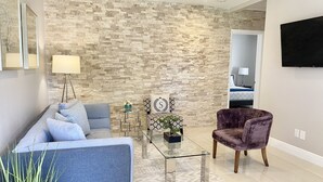 A modern living room with a stone wall, a blue sofa, a glass coffee table, and a purple armchair. - WEEKLY or MONTH TO MONTH LUXURY VACATION RENTAL - AP1  (Pompano Beach)