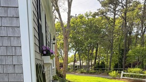 A landscaped garden with a variety of plants and a pathway leading to a house. - Walk to private beach, central air, wifi, 3 bedrooms. (Chatham)
