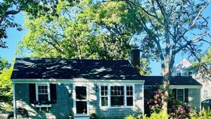 A single-story house with a front porch, a chimney, and a small garden with pink flowers. - Walk to private beach, central air, wifi, 3 bedrooms. (Chatham)