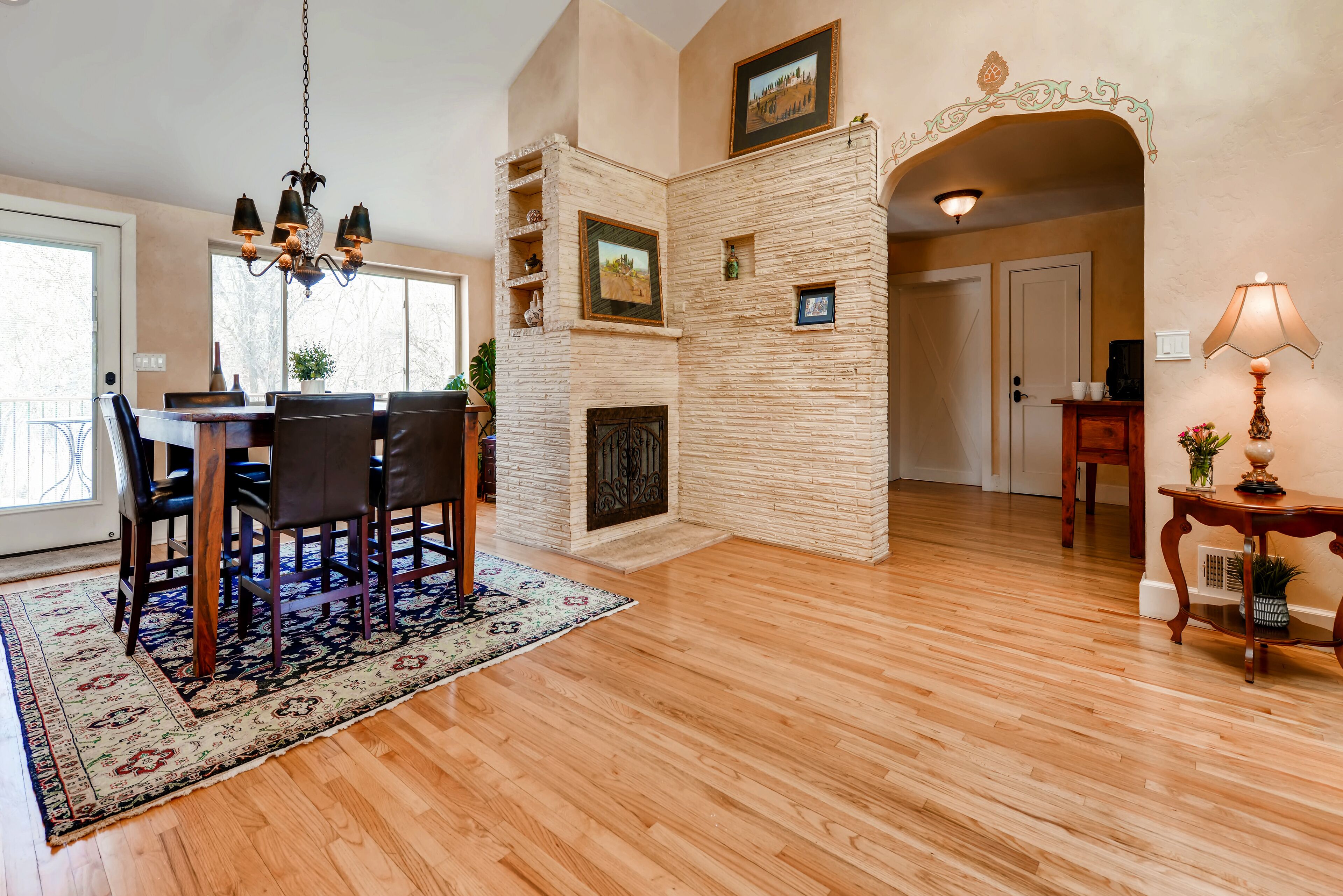 A dining area with a wooden table and chairs, a chandelier, a fireplace, and a view through a glass door.