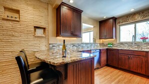 A kitchen with wooden cabinets, a stone backsplash, and a bar area with a black leather chair. - 3 Bedrooms - Gourmet Kitchen - Open Floorplan - Near Red Rocks & Near Downtown (Lakewood)