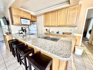 Eine Küche mit Granit-Arbeitsplatten, Holzschränken, einer Mikrowelle, einem Kühlschrank, einer Spüle und Barhocker.