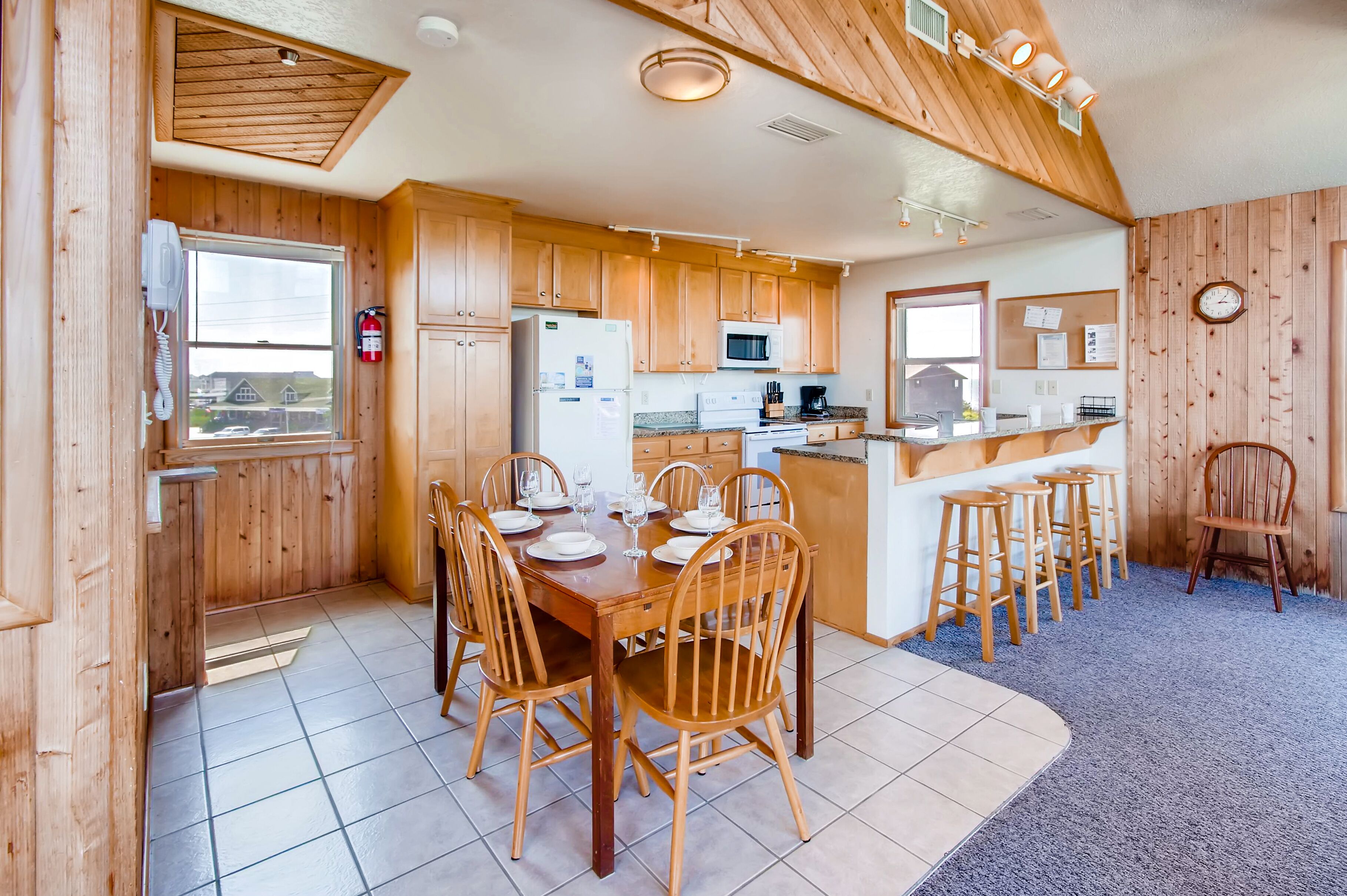 A wooden cabin-style kitchen with a dining table set for six, a refrigerator, microwave, and stove.