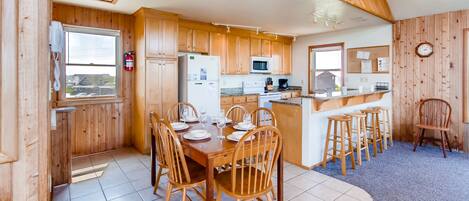 A wooden cabin-style kitchen with a dining table set for six, a refrigerator, microwave, and stove.