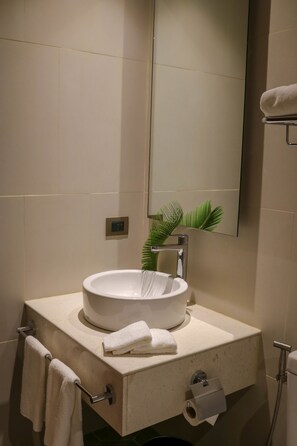 A bathroom with a white sink, a towel rack, a mirror, and a plant. - Acacia Hotel Bacolod (Bacolod)
