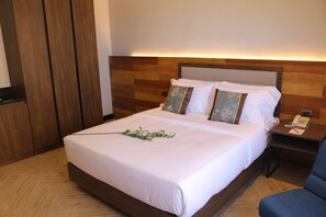 A neatly made bed with white linens, a wooden headboard, and a bedside table with a telephone and a notepad. - Acacia Hotel Bacolod (Bacolod)
