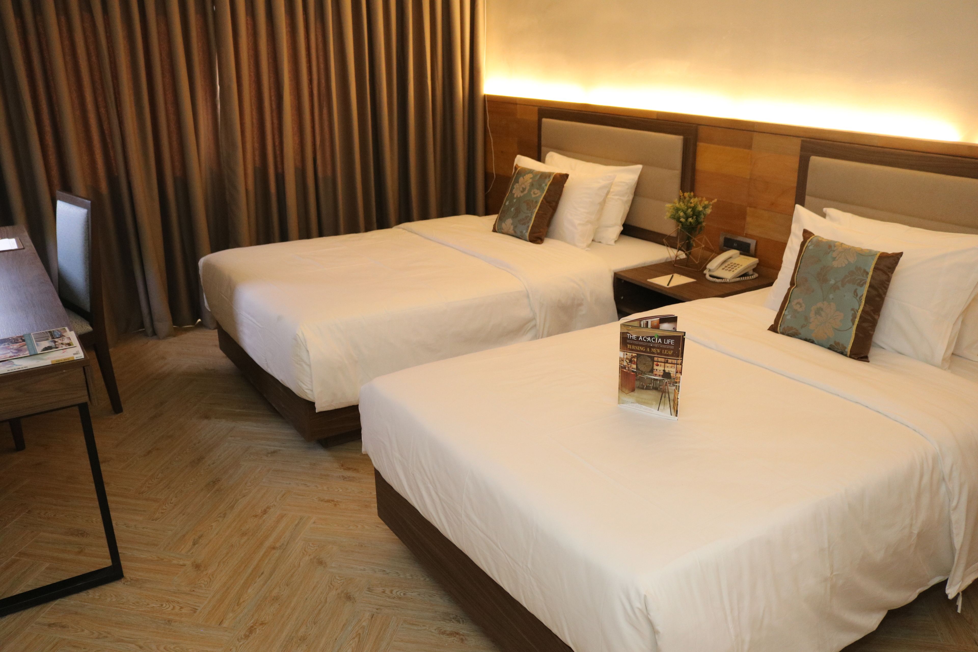 Habitación de hotel con dos camas, piso de madera, una mesita de noche con un teléfono y una revista sobre la cama.